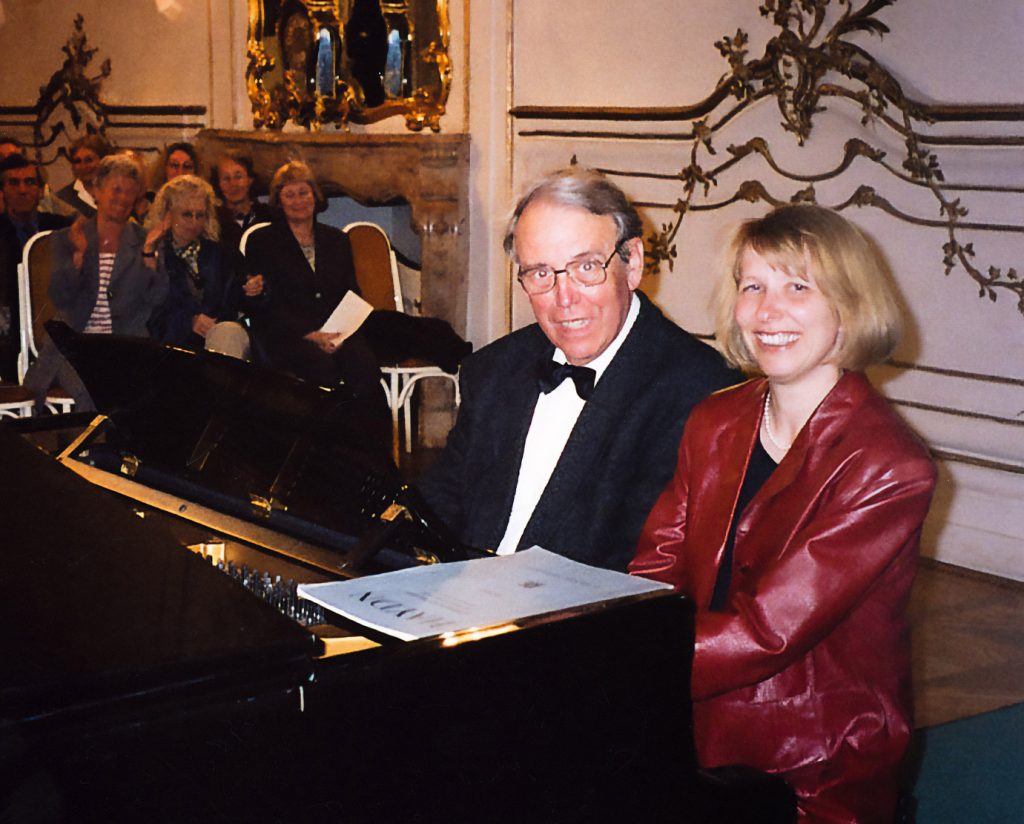 Detlef Wülbers und Heidi Schubert-Hornung posieren gemeinsam am Flügel sitzend, im Hintergrund Publikum.