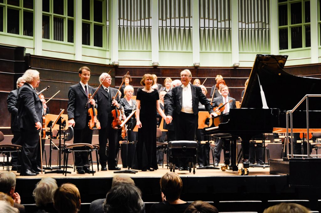 Heidi Schubert-Hornung und Dirigent Detlef Wülbers sowie das Orchester stehend beim Schlussapplaus.