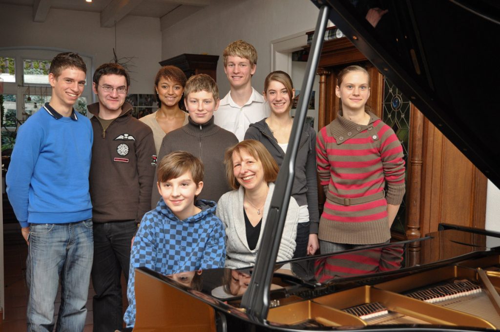 Gruppenfoto von Heidi Schubert-Hornung und acht jugendlichen Klavierschülern am Flügel.
